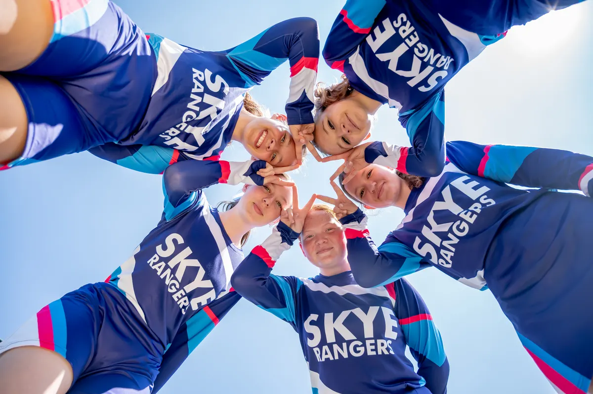 Skye College Rangers players in a huddle, seen from below against a blue sky