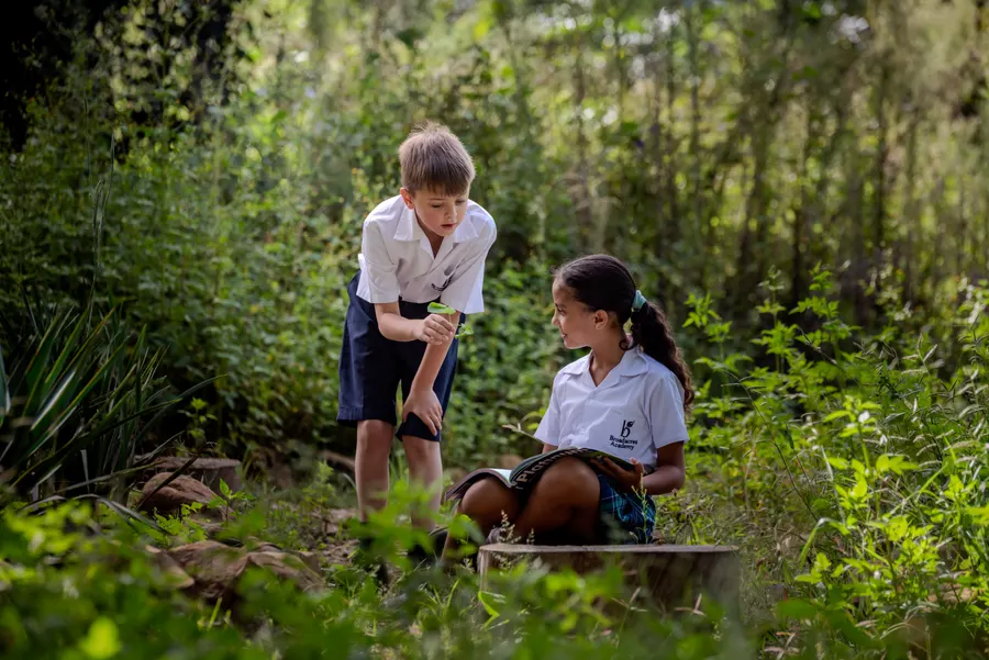 Two Broadacres Academy children reading together among green bushes