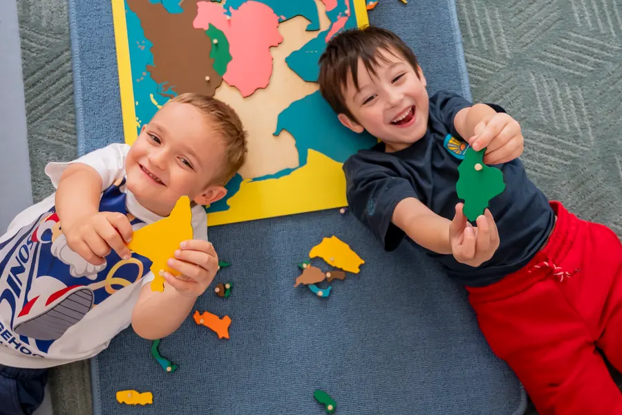 Two boys laughing on the floor with pieces of a map puzzle