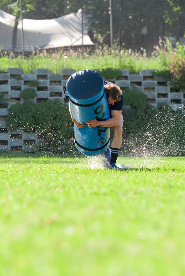 A Broadacres Academy child running with a rugby tackle bag through sprinkler spray